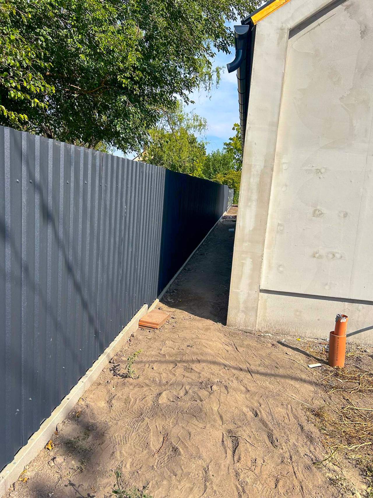 Antracit trapézlemez kerítés ház mellett – keskeny átjáró
