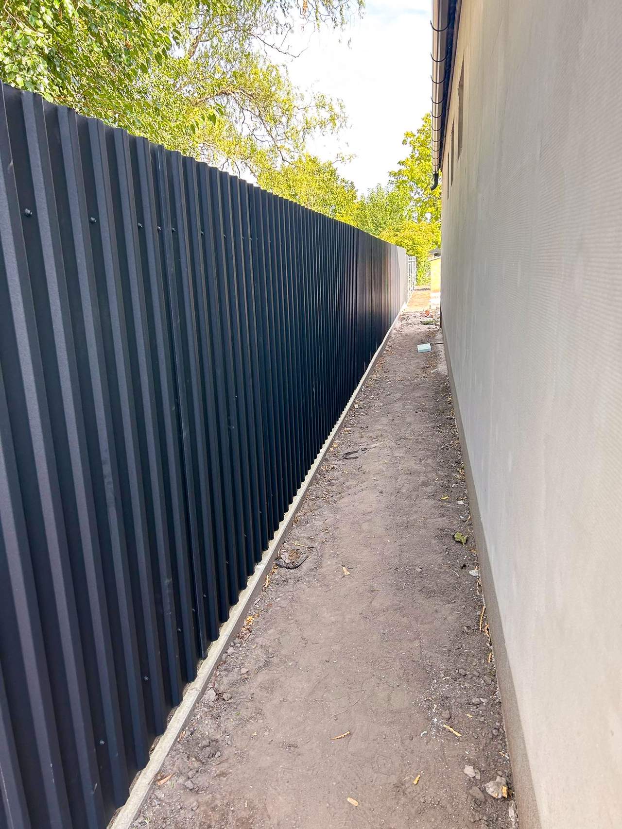 Antracit trapézlemez kerítés hosszú szakasza ház fal mellett